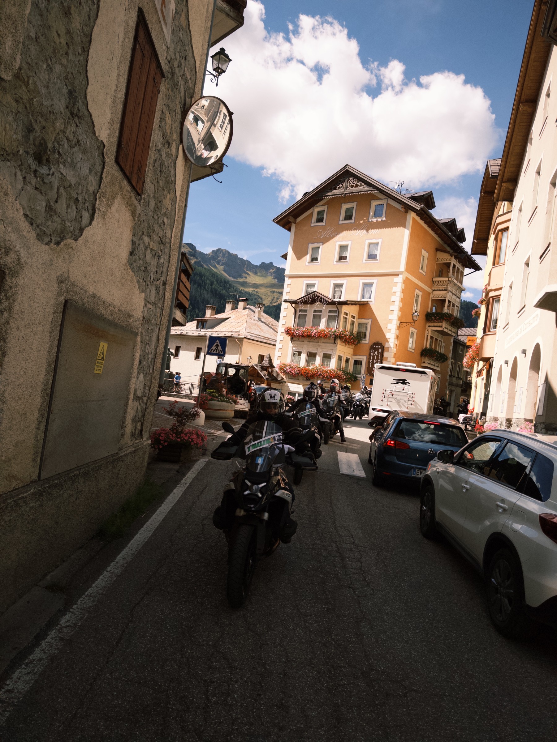 Moto na rua estreita de uma vila alpina, entre casas e carros