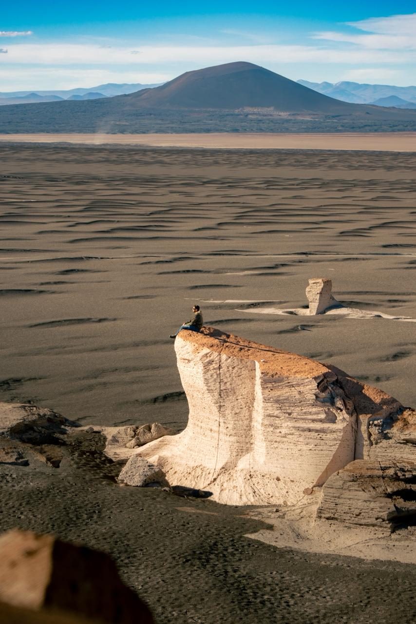 Deserto de altitude com formações rochosas e vulcão ao fundo