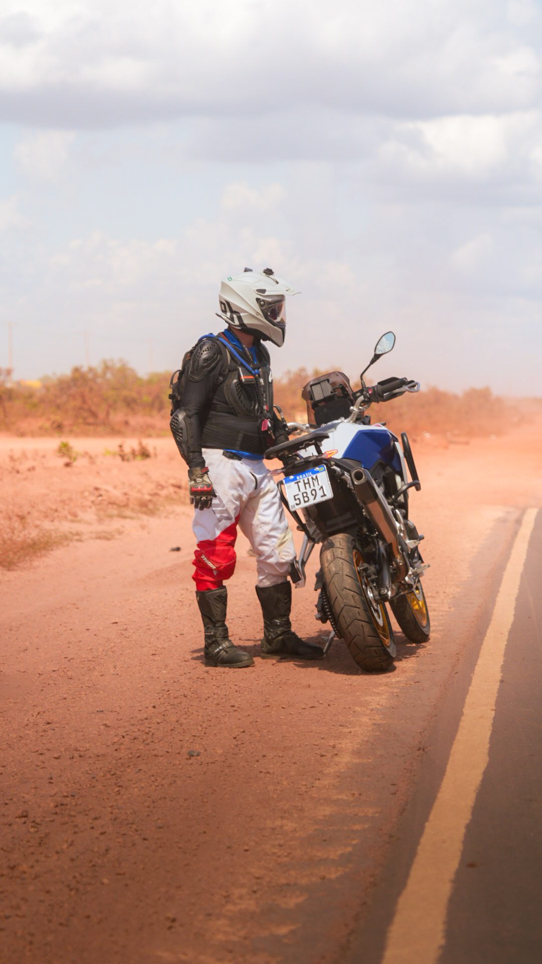 Piloto ao lado da moto em estrada de terra