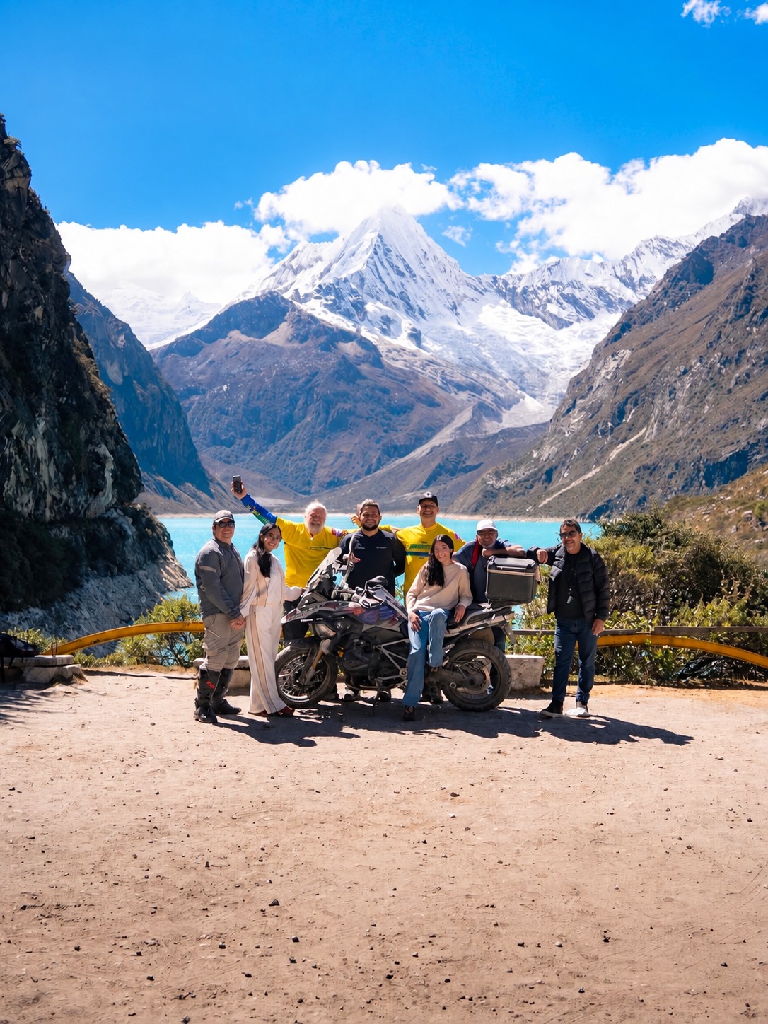 Grupo reunido em volta de uma moto diante da Laguna Parón e de picos nevados
